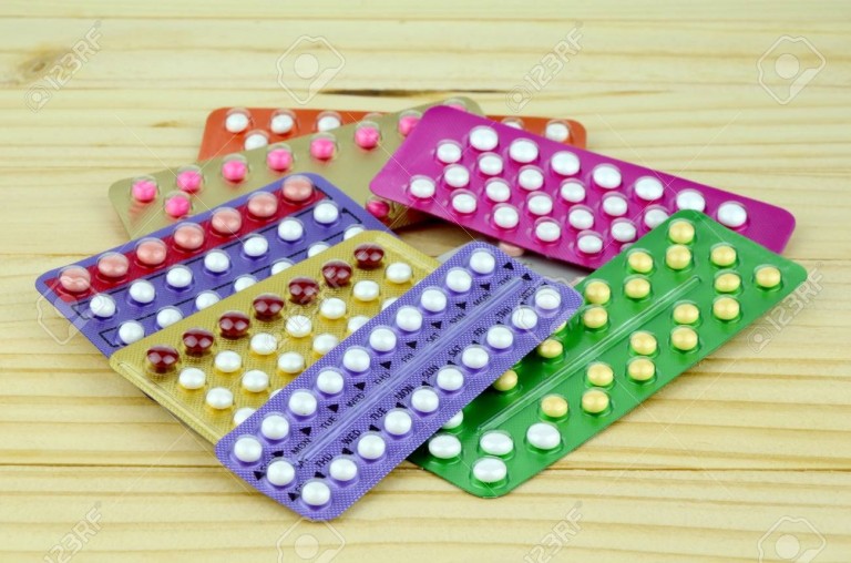 Colorful oral contraceptive pill strips on pine wood table.